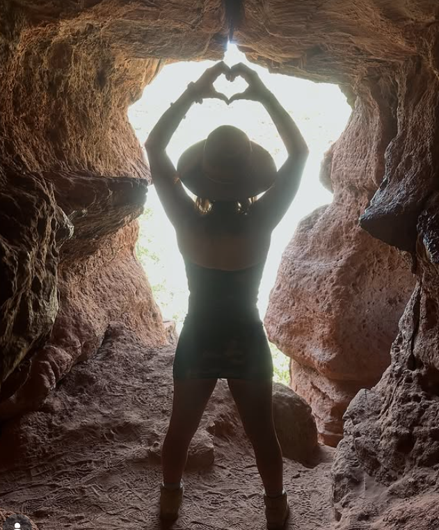 Making a heart with her hands in a sunlit canyon cave