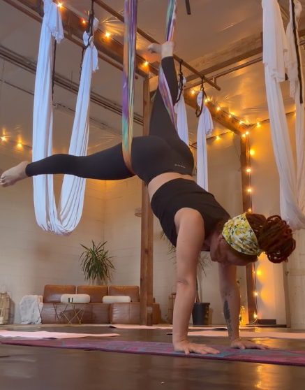 An aerial yoga pose under warm string lights in the studio