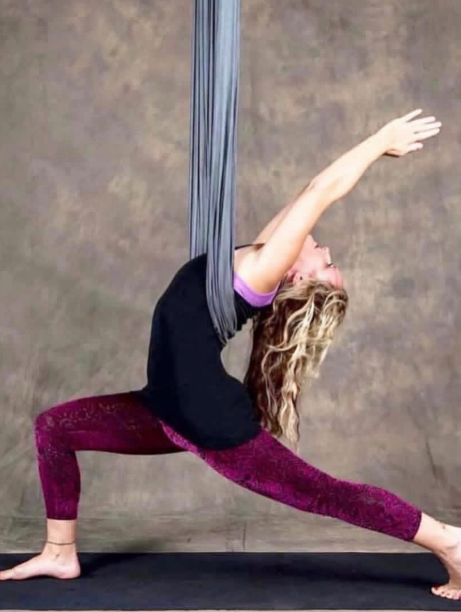A deep warrior stretch suspended in a grey aerial silk