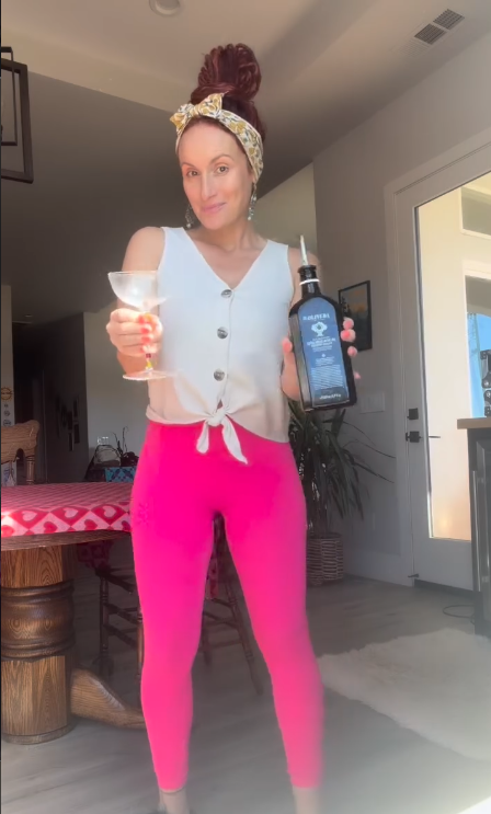 Christina toasting with an Oliveda bottle and a cocktail glass