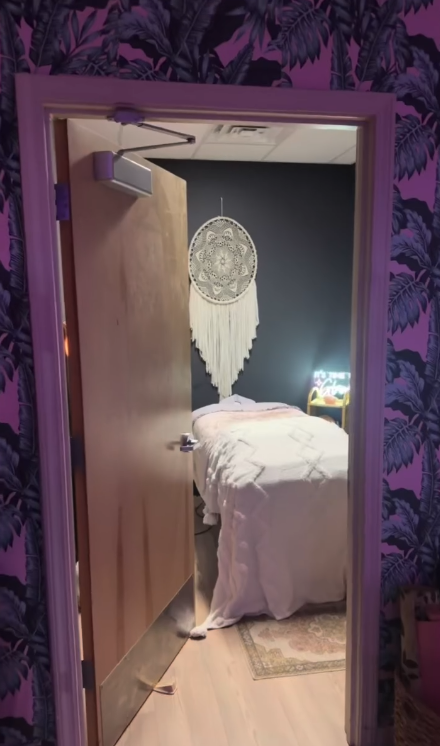 A doorway wrapped in purple floral wallpaper opening into the massage room